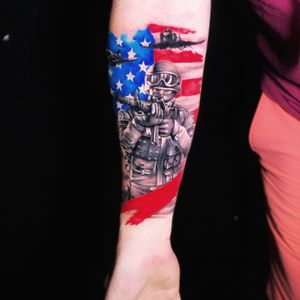 Capture the essence of bravery with this forearm tattoo by Marcel Oliveira, showcasing a soldier, flag, and airplane in a stunning mix of realism and trashpolka style.