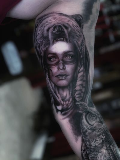 Stunning black and gray upper arm tattoo featuring a bear, owl, and woman, by the talented Marcel Oliveira.
