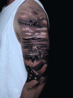 A bold blackwork piece on the upper arm featuring a car, airplane, and soldier in a realistic and illustrative style by Marcel Oliveira.