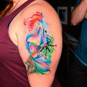 Illustrative upper arm tattoo featuring a colorful anchor with a silhouette of a woman, created by artist Marcel Oliveira.