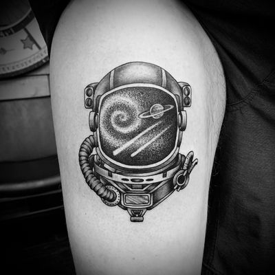 Explore the cosmos with this blackwork traditional tattoo featuring a helmet amidst planets on your upper arm. By artist Jose Cordova.