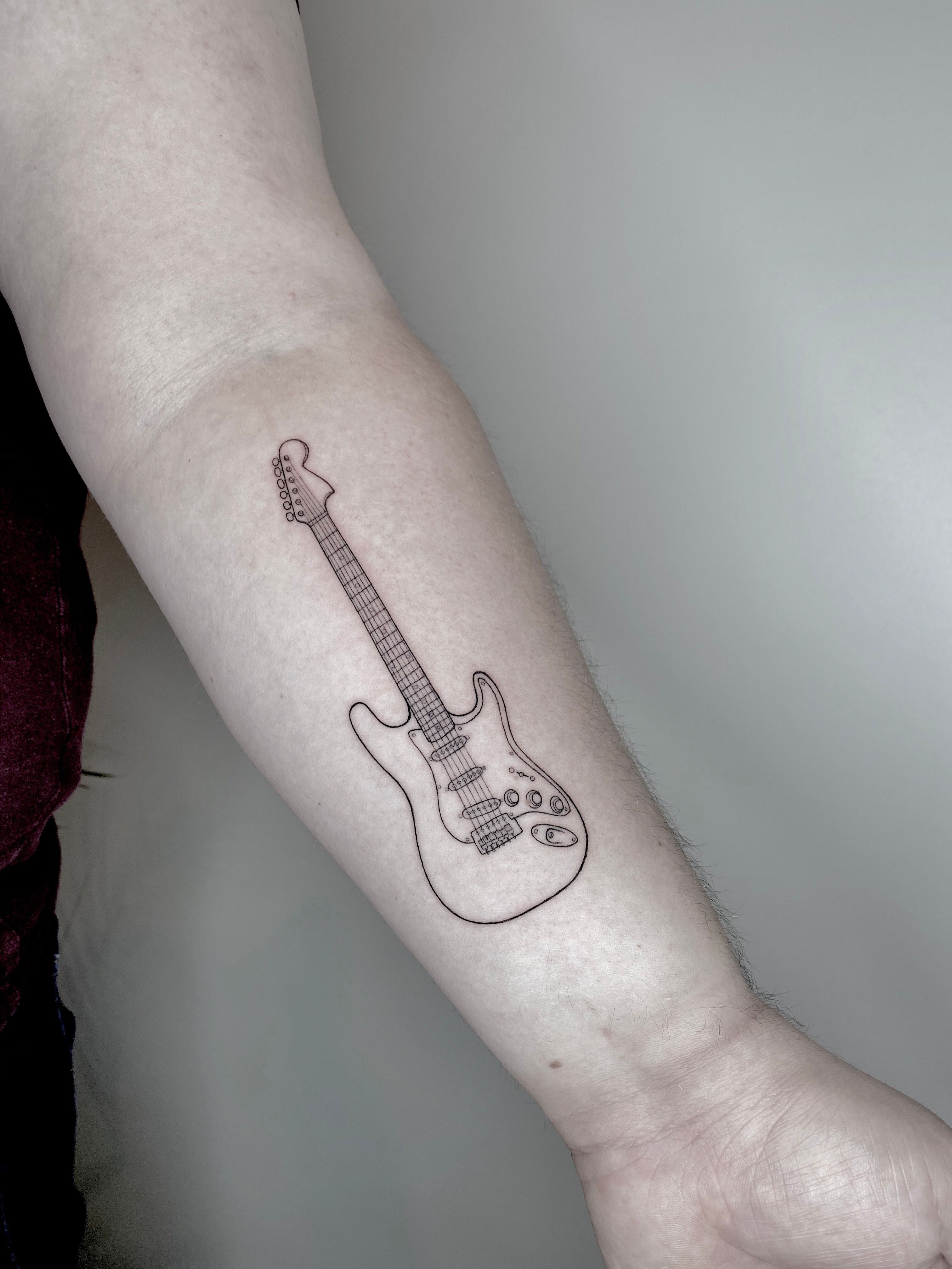 A very small tattoo of a black and grey guitar on forearm on Craiyon