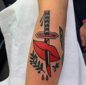 Illustrative forearm tattoo in London featuring a sword with bloody lips and a sprig motif.