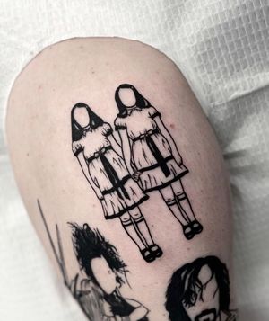 Get a spine-chilling blackwork tattoo of twin girls on your upper arm by the talented artist Miss Vampira.