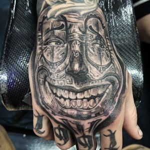 Get inked by Jake Masri with a stylish black and gray design featuring a man and clown motif on your hand.