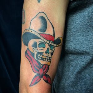 Check out this impressive arm tattoo featuring a traditional style skull wearing a cowboy hat, done by the talented artist Felipe Reinoso.