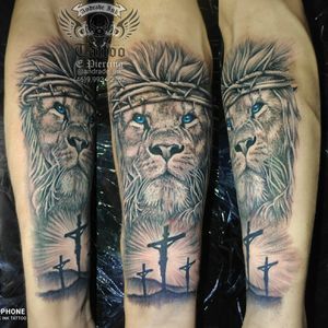 Tatuagem leão realista com coroa de espinhos e cruzes com Jesus crucificado, no antebraço masculino
