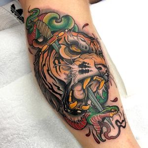Experience the fierce beauty of a neo-traditional snake and tiger design by Jethro Wood, featuring a dagger dripping with blood. Perfect for those who crave bold and intricate body art.