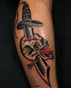 Bold traditional design by Felipe Reinoso on lower leg. Combining skull and sword motifs for a powerful statement.
