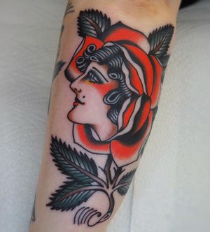 Get a timeless traditional tattoo of a beautiful woman surrounded by flowers on your forearm in London, GB.