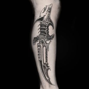 Get a unique black and gray tattoo of a shark and dagger on your lower leg in London. Perfect for those who love marine life and edgy designs.