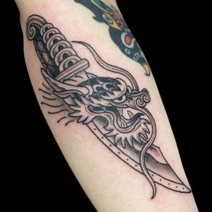 Get a fierce and traditional Japanese dragon dagger tattoo on your forearm in London, GB. Expertly done in black and gray style.