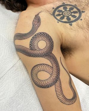 Check out this sleek black and gray fine line snake tattoo on the upper arm, done by talented artist Sophie Rose Hunter.