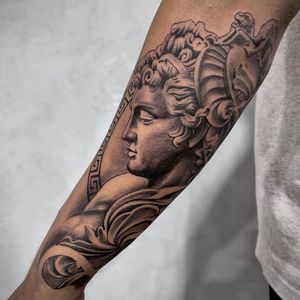 Get a striking black and gray illustrative tattoo of a man statue with intricate filigree details on your forearm in Los Angeles.