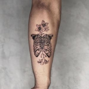 Get a stunning blackwork tattoo of a flower intertwined with a skull and skeleton on your forearm. Visit our studio in Los Angeles!