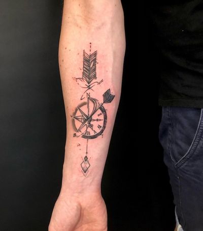 Black and gray fine line tattoo on forearm, featuring a compass and arrow design by Sandro Secchin.