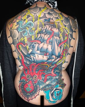 Full back tattoo featuring a kraken, ship and a little moon face blowing a storm around.  Most of the tattoo is healed and settled over a year (thanks, global pandemic).  We were finally able to finish up coloring the sails after the client and I were both vaccinated.  