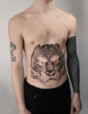 Get inked with a fierce black and gray tiger design by FKM TATTOO. Perfect for those wanting a bold and unique stomach piece.