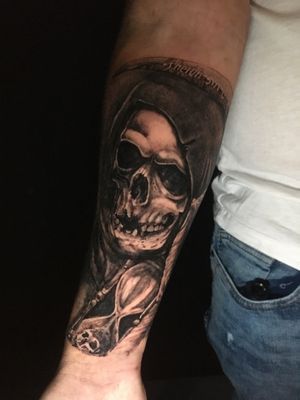 Frankie Brown's blackwork realism forearm tattoo featuring a skull and hourglass motif.