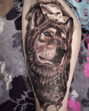 Experience the ethereal beauty of this black and gray realism tattoo featuring a majestic wolf under the glow of the moon on your upper leg.