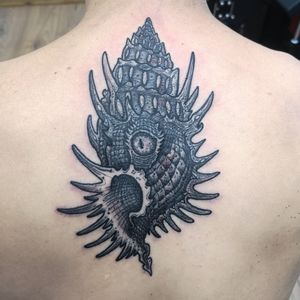 Adorn your upper back with a stunning black and gray shell tattoo by Fernando Joergensen. Embrace the beauty of the sea with this delicate design.