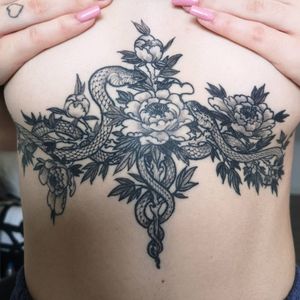 Underboob tattoo by Fernando Joergensen featuring a snake intertwined with a delicate flower in black and gray floral style.