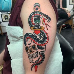 Get inked by the talented Andrea Furci with this bold and edgy upper arm design featuring a snake, skull, and dagger in traditional style.