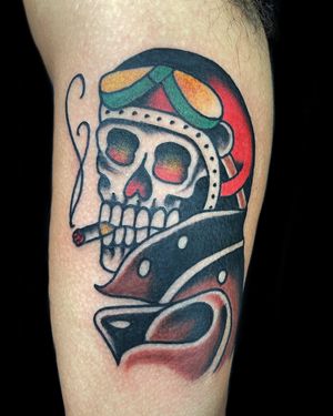Get an edgy traditional tattoo with a skull, goggles, cigarette, and helmet design on your upper arm by Felipe Reinoso.