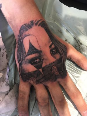Check out this stunning black and gray tattoo by artist Frankie Brown featuring a realistic girl and clown design on the hand.