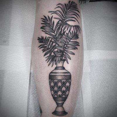 A stunning black and gray dotwork tattoo on the lower leg. Features a vase filled with intricate leaf designs, expertly done by Lamat.
