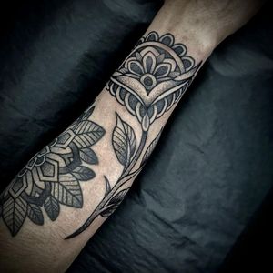 Elegant black and gray forearm tattoo by Lamat, featuring a intricate floral mandala design with delicate dotwork elements.
