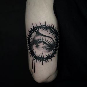 A striking black and gray tattoo featuring an intricate eye surrounded by thorns and eyebrow details, expertly done by Lamat.