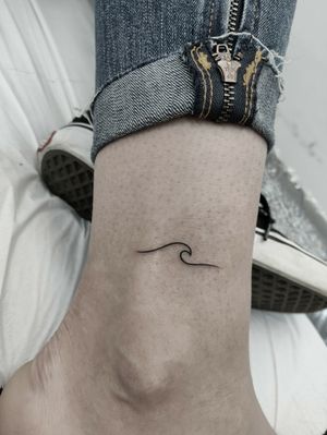 Elegantly designed fine line wave tattoo on the ankle by Mary Shalla. Perfect for ocean lovers.