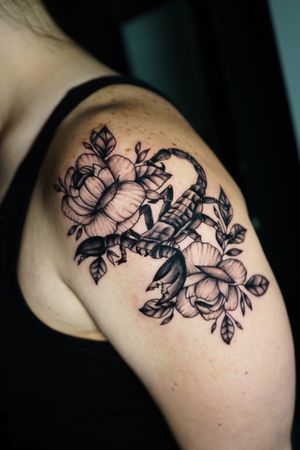 Unique blackwork tattoo on upper arm by Miss Vampira, combining a fierce scorpion with delicate flower details.