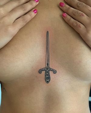 Illustrative blackwork sword tattoo by Brigid Burke, delicately etched on sternum for a powerful and unique aesthetic.