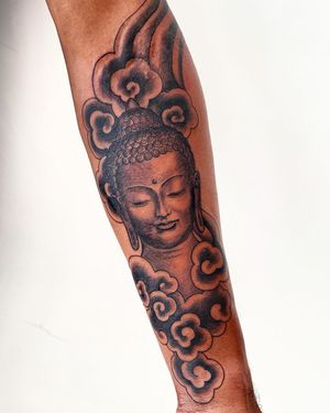 Exquisite blackwork tattoo of Buddha among serene clouds on forearm by Brigid Burke.