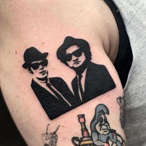 Get inked with a classic tattoo featuring a man in a hat and glasses, expertly done by Miss Vampira on your upper arm. Stand out with this timeless design.