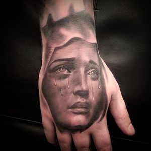 Express your emotions with a striking black and gray tattoo of a woman shedding tears, perfect for your hand. Located in London, GB.