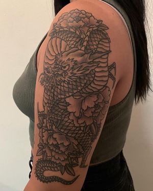 A stunning blackwork tattoo by Shawn Nutting featuring a fierce dragon and delicate flower design on the upper arm