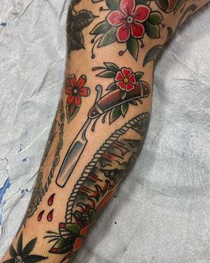 Get a bold and vibrant traditional tattoo featuring a mix of delicate flowers and sharp razor blade, perfect for your lower leg. Located in Los Angeles, US.