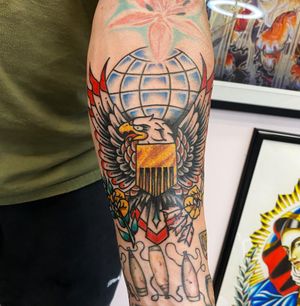 Impressive traditional tattoo featuring an eagle soaring over a world map, expertly done by artist Andre Bertoncin.