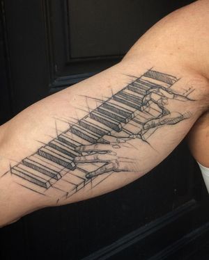 Beautiful fine line tattoo on upper arm featuring a realistic piano, hand, and keyboard motif by artist Aygul.