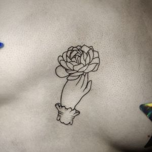 Beautiful fine line tattoo featuring a delicate flower and hand design by artist Mary Shalla on the sternum area.