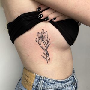 Elegant and detailed dotwork and fine line design of a flower and sprig, artfully crafted by Chris Harvey on the ribs. Perfect for a delicate and unique tattoo.