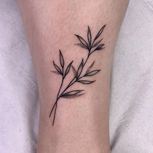 Fine line arm tattoo by Chris Harvey featuring a delicate floral sprig and leaf motif.