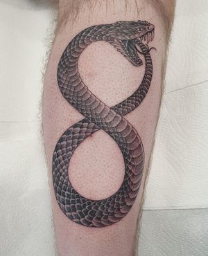 Blackwork illustrative design by Dani Mawby, depicting a serpent biting its own tail on lower leg.