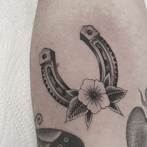 Beautiful arm tattoo featuring a flower and horseshoe motif, expertly designed by Dani Mawby.
