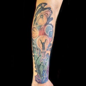Illustrative tattoo on forearm featuring a planet, bulb, lamp, and hand by Michaelle Fiore.