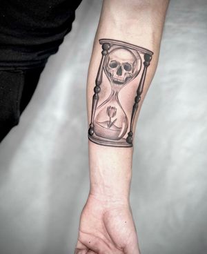 Unique forearm tattoo in blackwork style featuring a flower, skull, and hourglass motif. Located in Los Angeles.