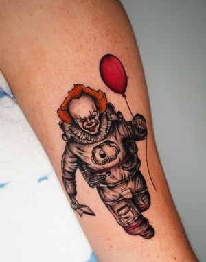 Unique forearm tattoo featuring a mix of astronaut, clown, and pennywise motifs by Miss Vampira. A surreal and illustrative design.